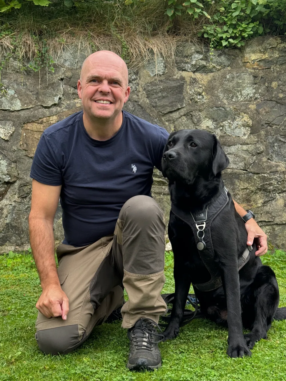 Rob kneler på gresset ved siden av den svarte labradoren Baloo